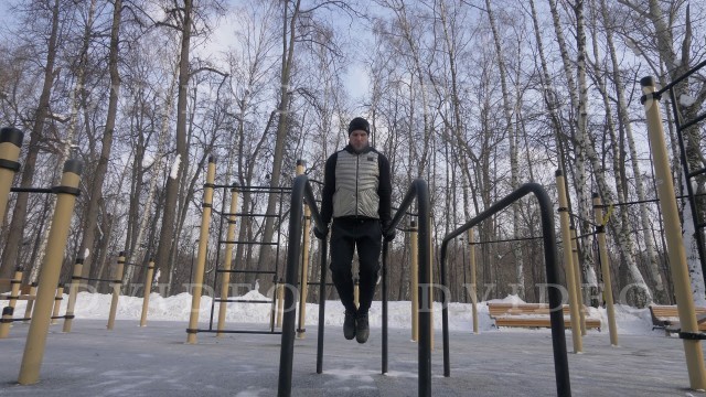 'Fitness man training push ups exercise on bar on winter sport ground'